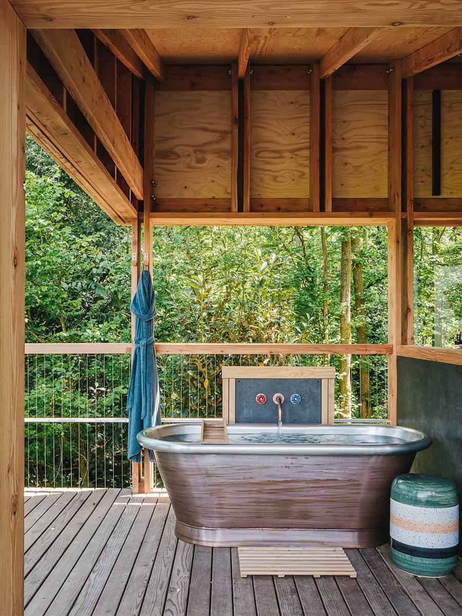 Freestanding copper bathtub on outdoor deck at Elmore Treehouses surrounded by woodland canopy